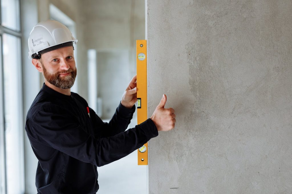 pexels-photo-8482816 Confident male construction worker using a spirit level on a concrete wall for precise alignment indoors.